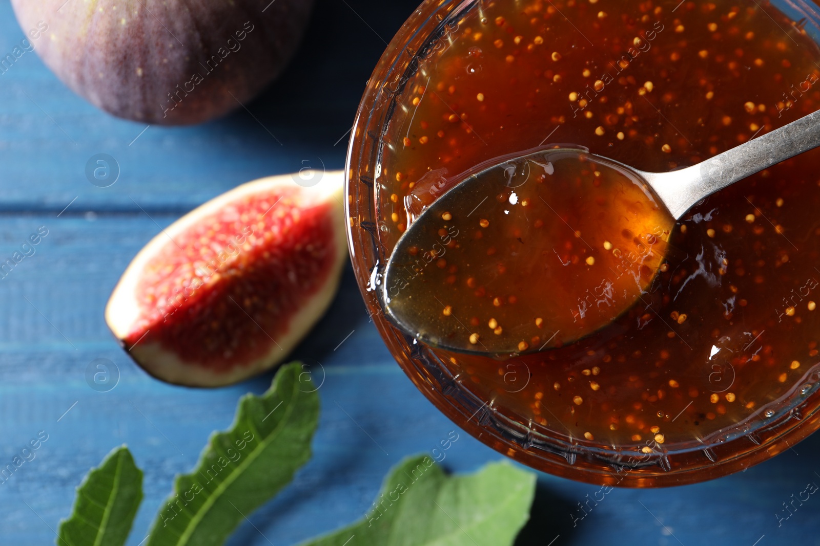 Photo of Glass bowl with tasty sweet jam and fresh figs on blue wooden table, flat lay. Space for text