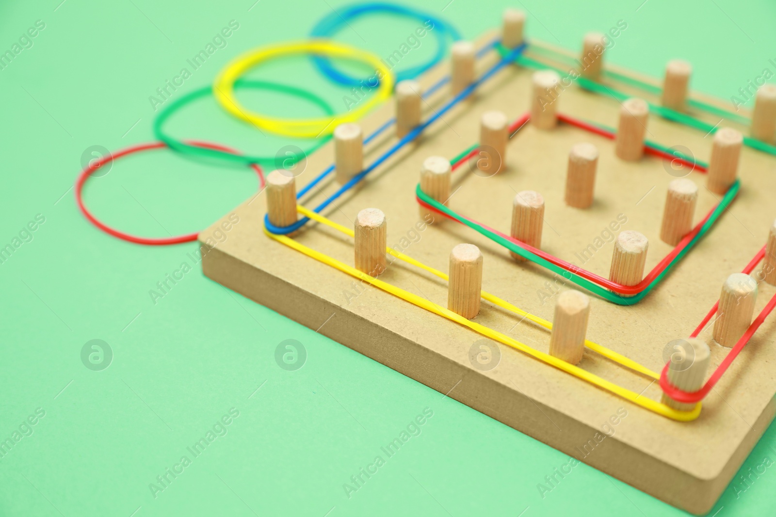 Photo of Wooden geoboard with rubber bands on green background, closeup with space for text. Educational toy for motor skills development