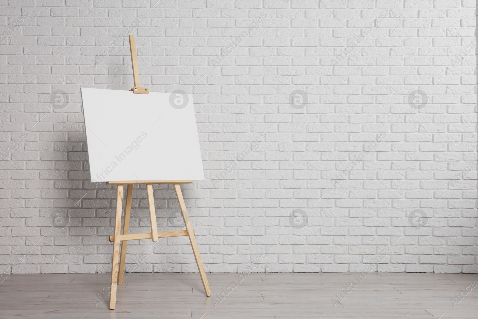 Photo of Wooden easel with blank canvas near white brick wall indoors. Space for text