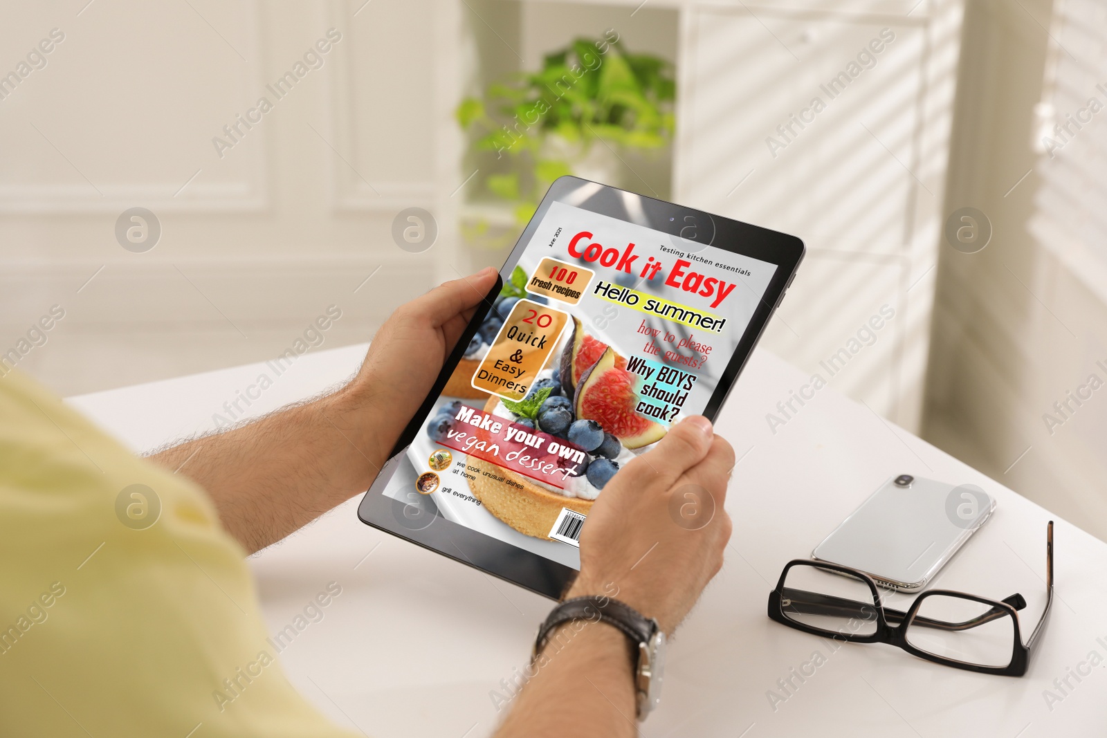 Photo of Man reading online magazine on tablet at white table, closeup