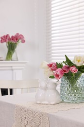 Easter decorations. Bouquet of tulips in vase and bunny figures on white table at home