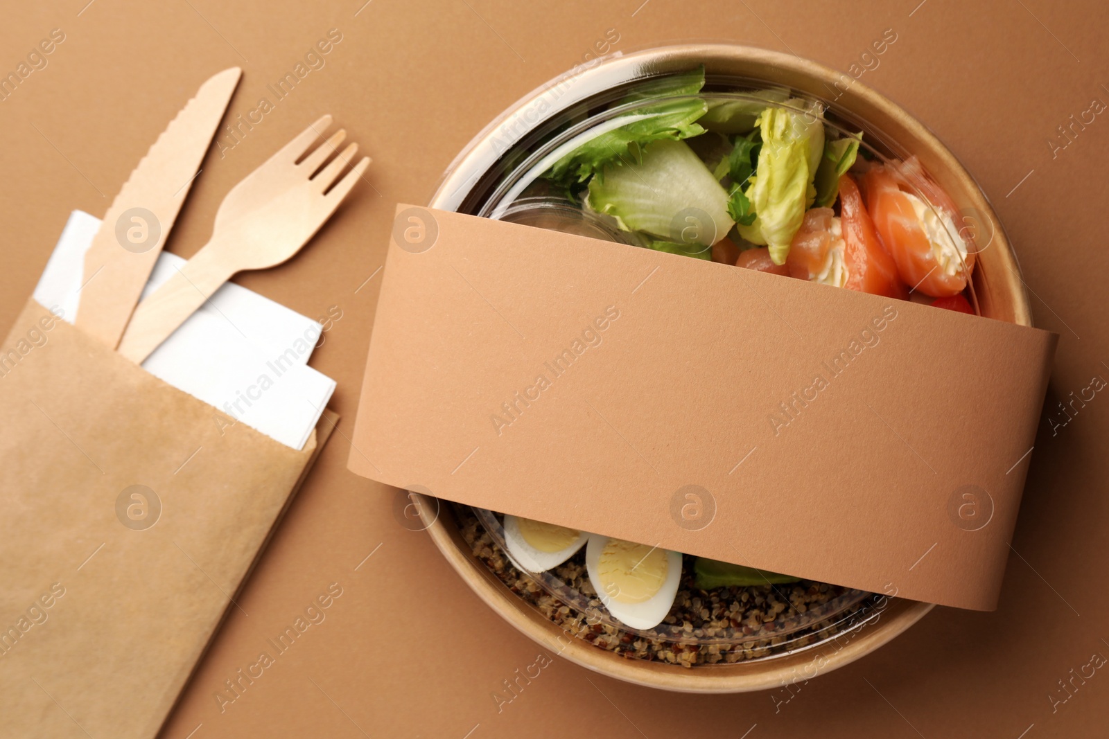 Photo of Tasty food in container with wooden fork and knife on beige background, flat lay. Space for text