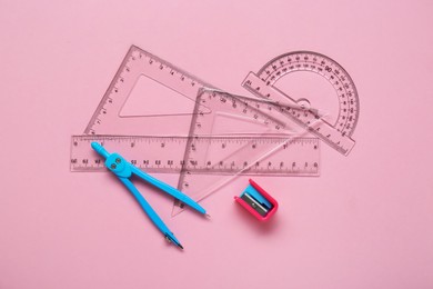 Different rulers, pencil sharpener and compass on pink background, flat lay