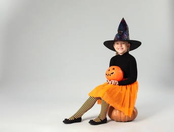 Photo of Cute little girl with pumpkin candy bucket wearing Halloween costume on grey background. Space for text