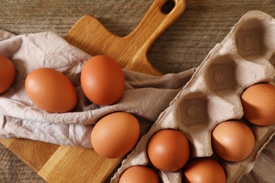 Raw chicken eggs with carton, napkin and board on wooden table, flat lay