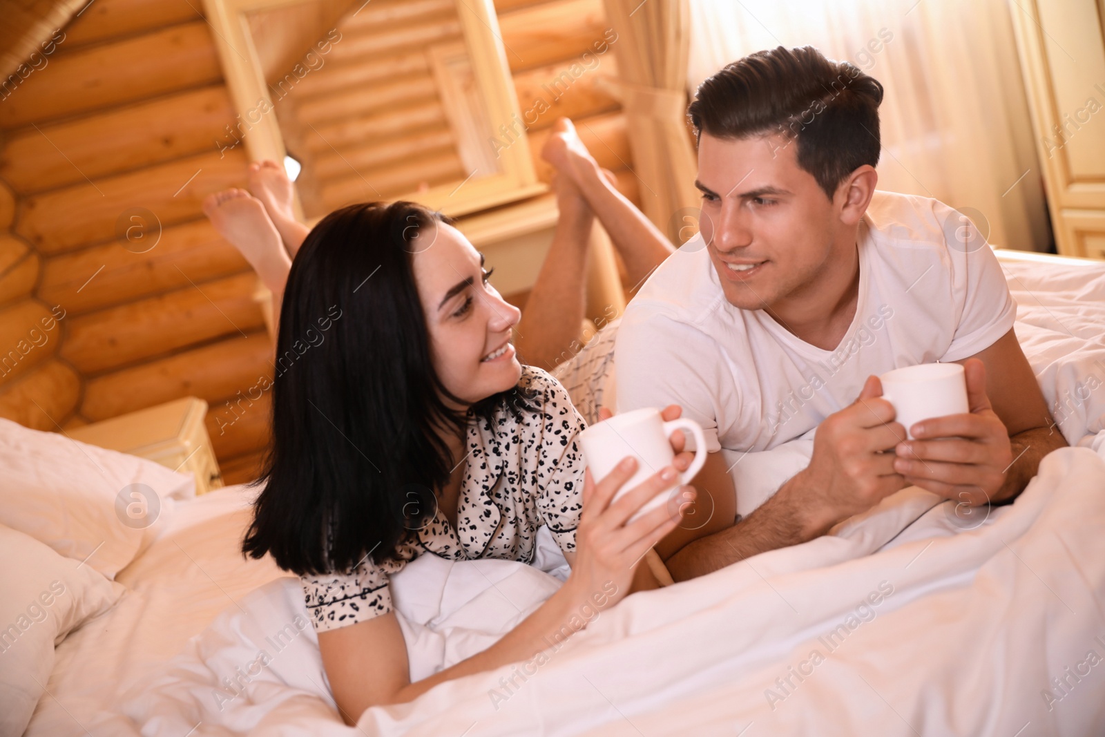 Photo of Couple with drinks lying in bed at home. Lazy morning