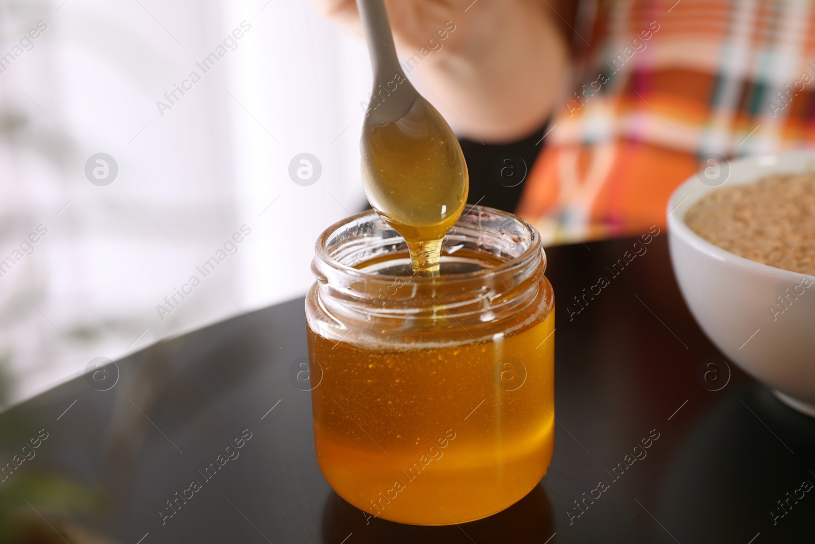 Photo of Spoon with honey over jar on black table, closeup