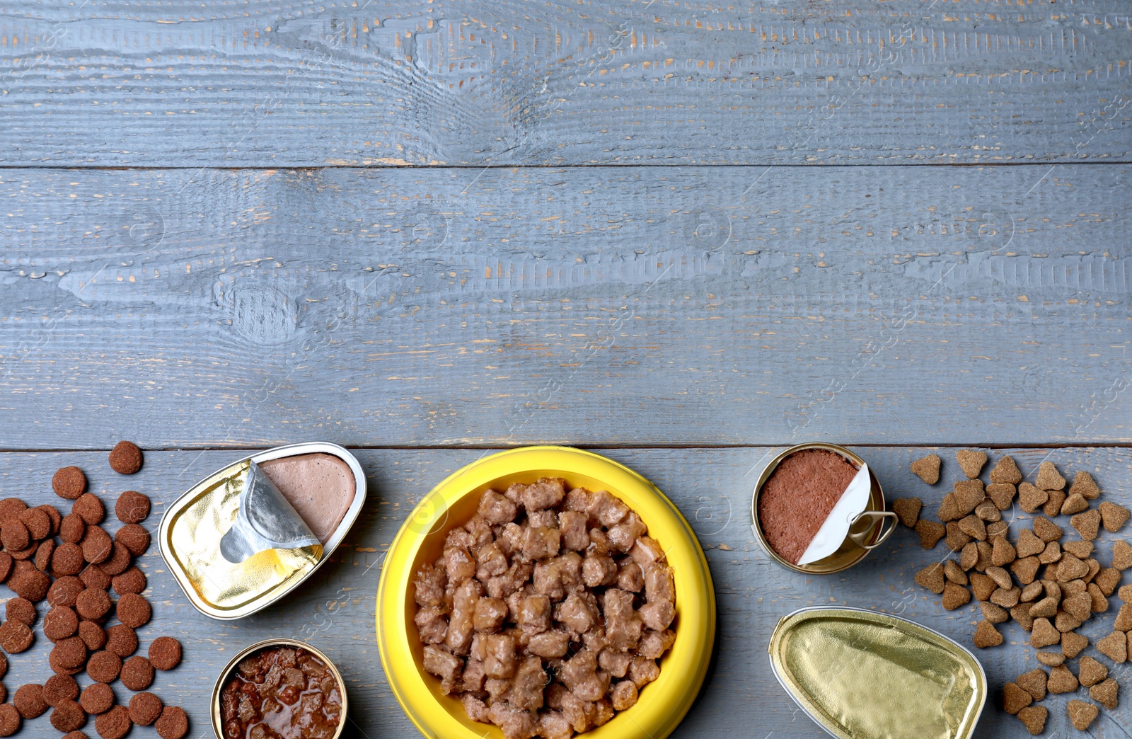 Photo of Wet and dry pet food on blue wooden table, flat lay. Space for text