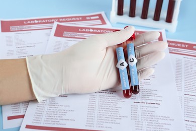 Photo of Scientist holding tubes with blood samples for hepatitis virus test near laboratory form, closeup