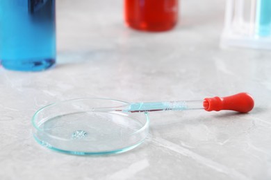 Photo of Glass pipette and petri dish with liquid on grey marble table, closeup