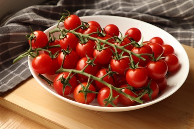 Photo of Plate of ripe whole cherry tomatoes on wooden table, closeup