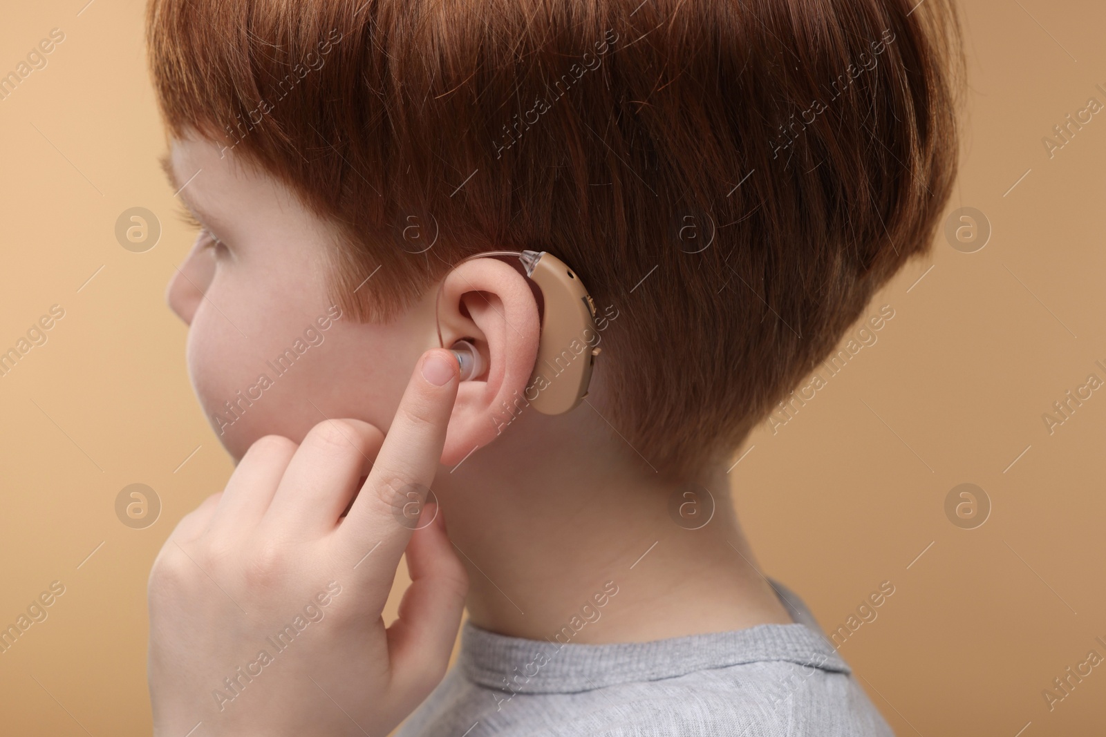 Photo of Little boy with hearing aid on pale brown background, closeup