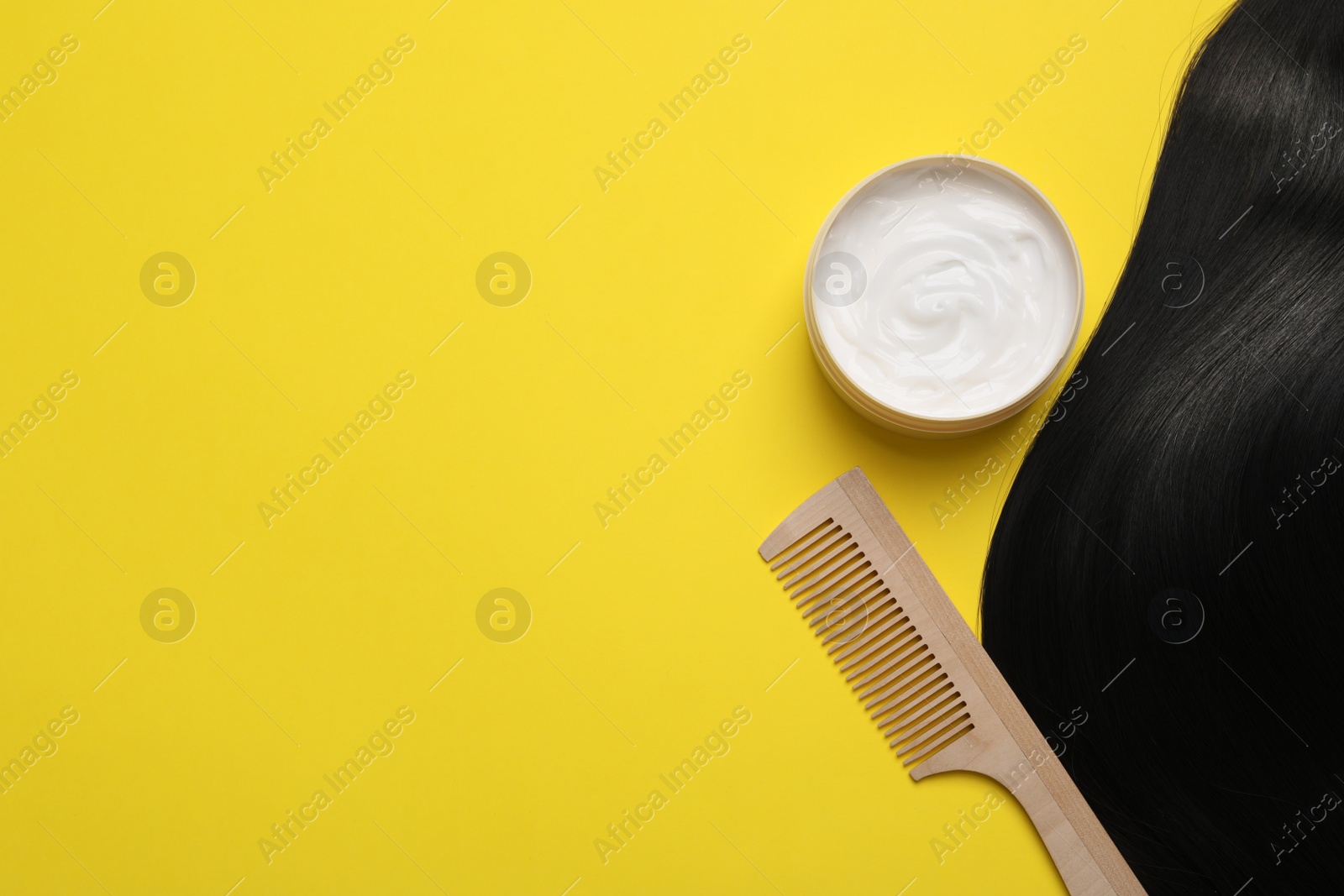 Photo of Lock of healthy black hair, cosmetic product and comb on yellow background, flat lay. Space for text