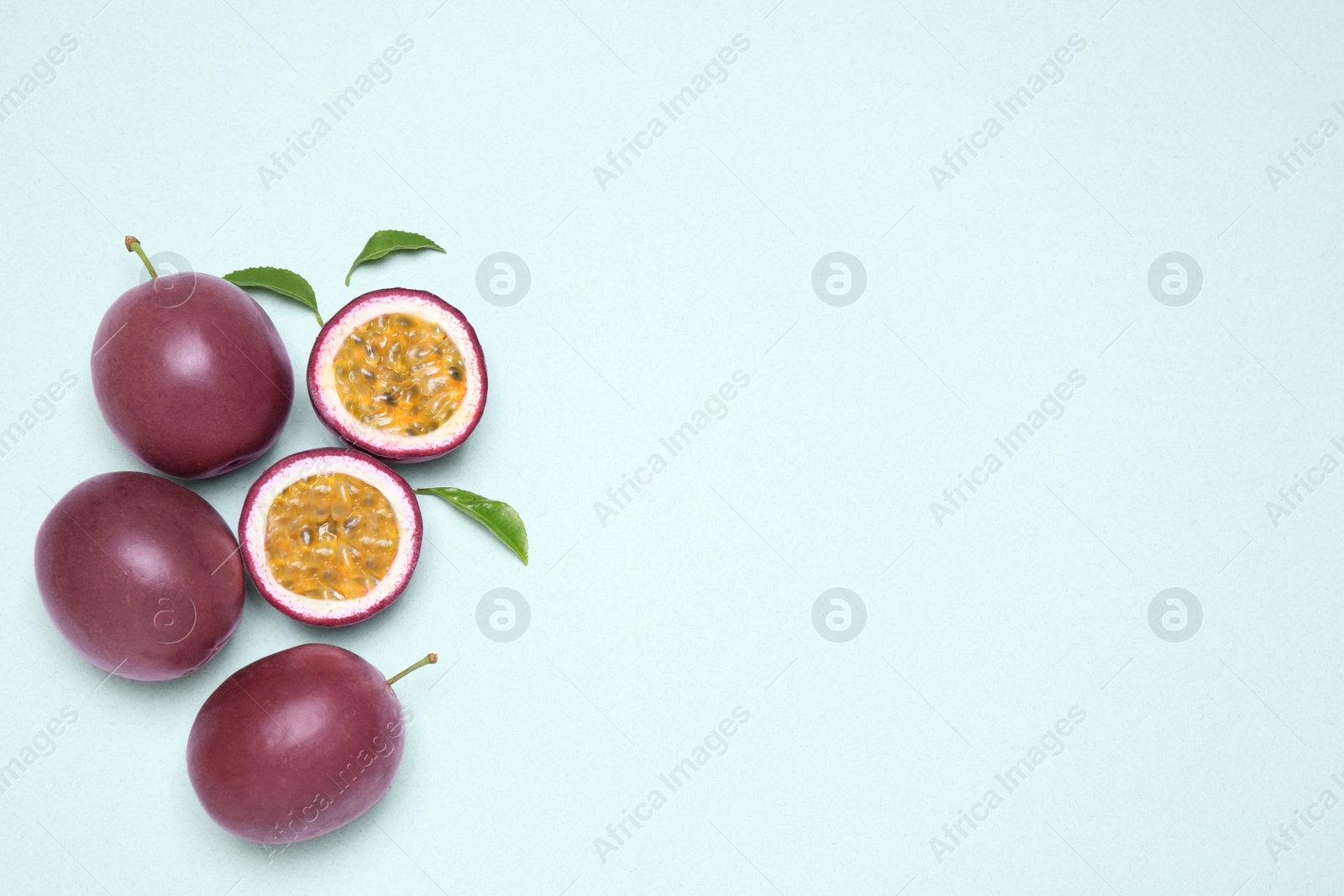 Photo of Fresh ripe passion fruits (maracuyas) with leaves on light background, flat lay. Space for text