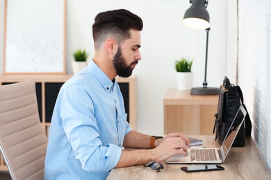 Photo of Handsome young man working with laptop at table in home office