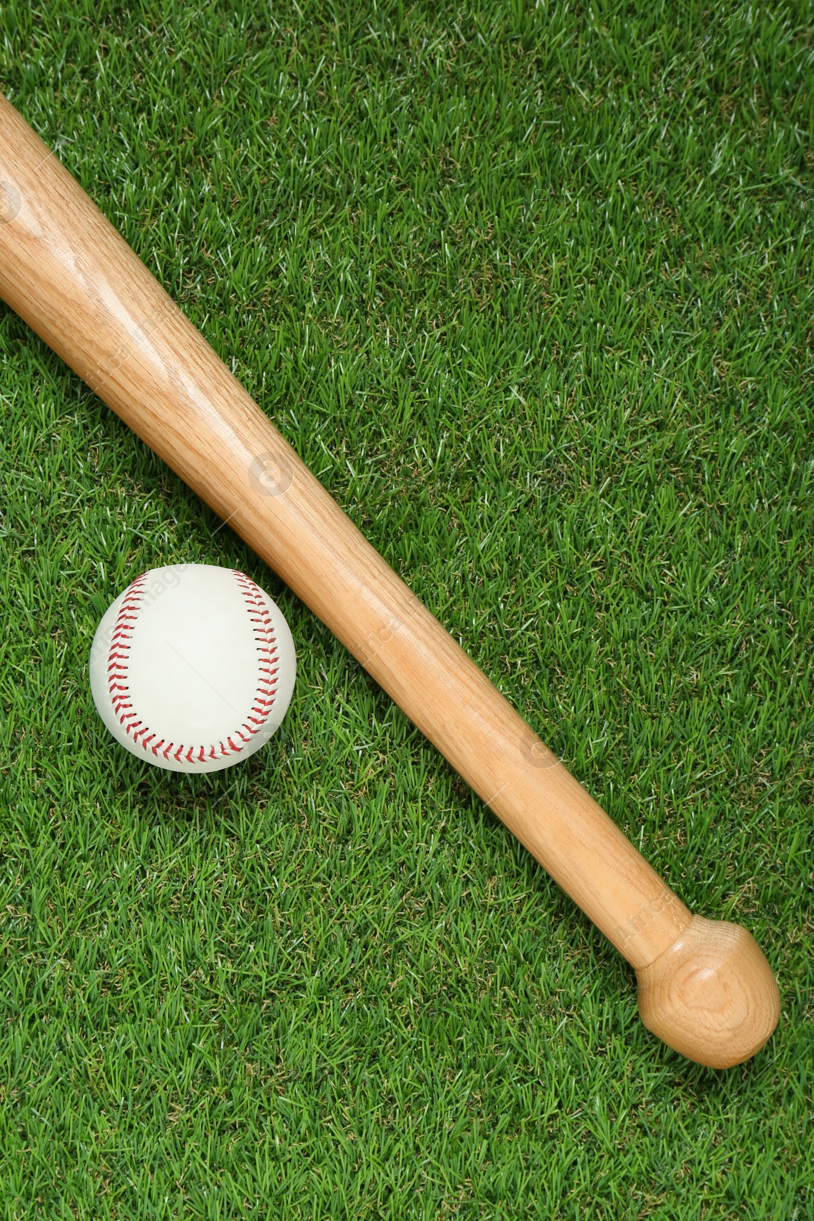 Photo of Wooden baseball bat and ball on green grass, flat lay. Sports equipment