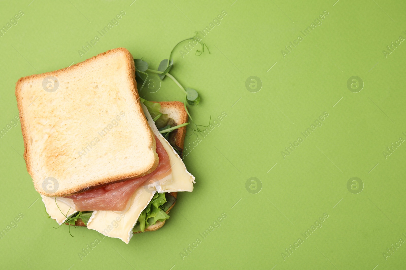 Photo of Tasty sandwich with brie cheese and prosciutto on light green background, top view. Space for text