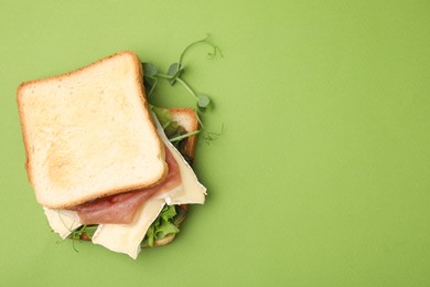 Tasty sandwich with brie cheese and prosciutto on light green background, top view. Space for text