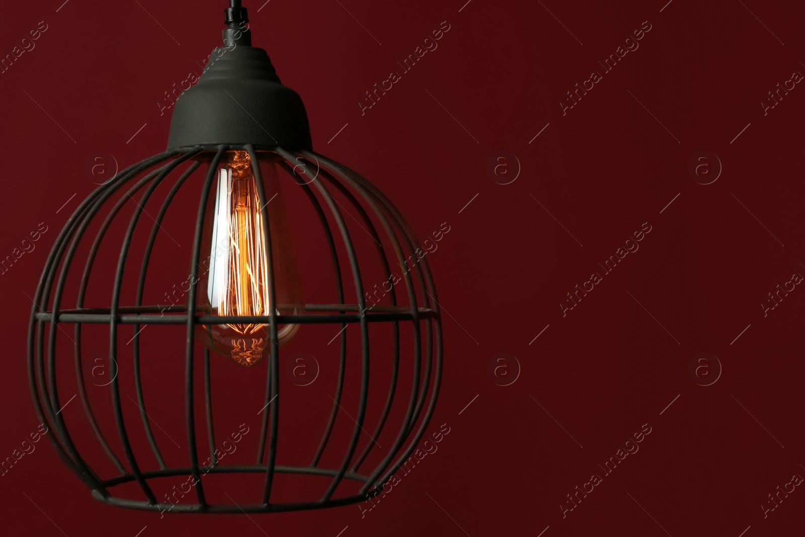 Photo of Hanging lamp bulb in chandelier against dark red background, space for text