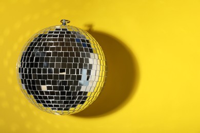 Photo of Shiny disco ball on yellow background, top view. Space for text