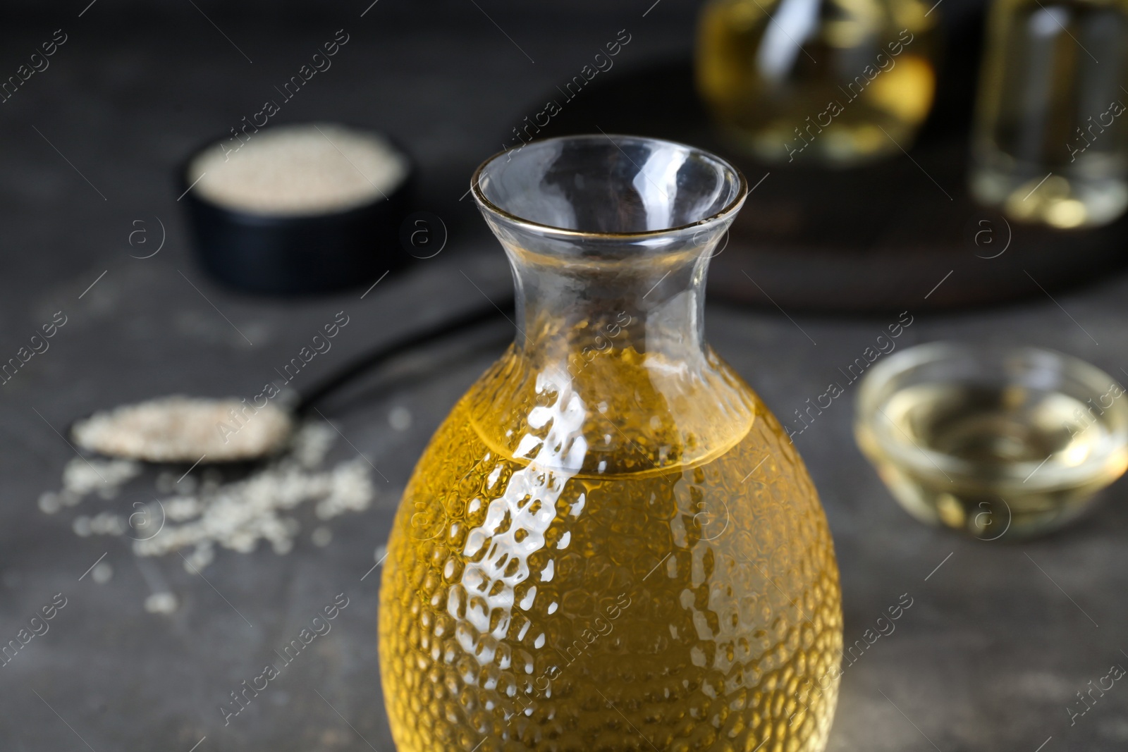 Photo of Fresh sesame oil in glass bottle on grey table, closeup