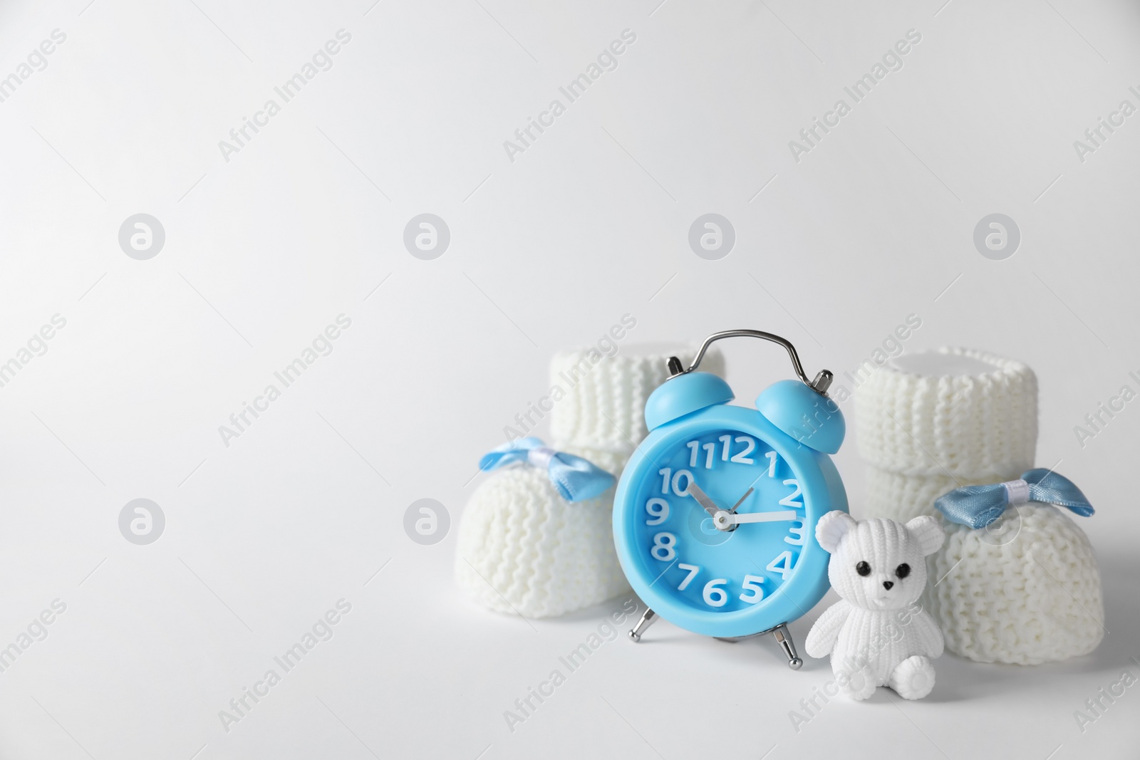 Photo of Alarm clock, toy bear and baby booties on white background, space for text. Time to give birth