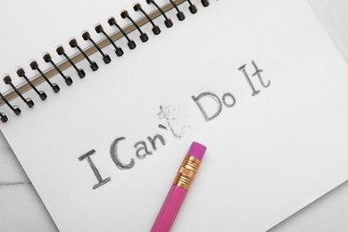 Photo of Motivation concept. Notebook with changed phrase from I Can't Do It into I Can Do It by erasing letter T on white table, top view