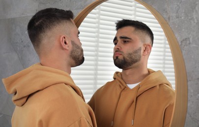 Sad young man near mirror at home