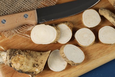 Photo of Board with cut horseradish root and knife on table, top view