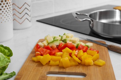 Photo of Wooden board with cut vegetables and knife near saute pan in kitchen, closeup
