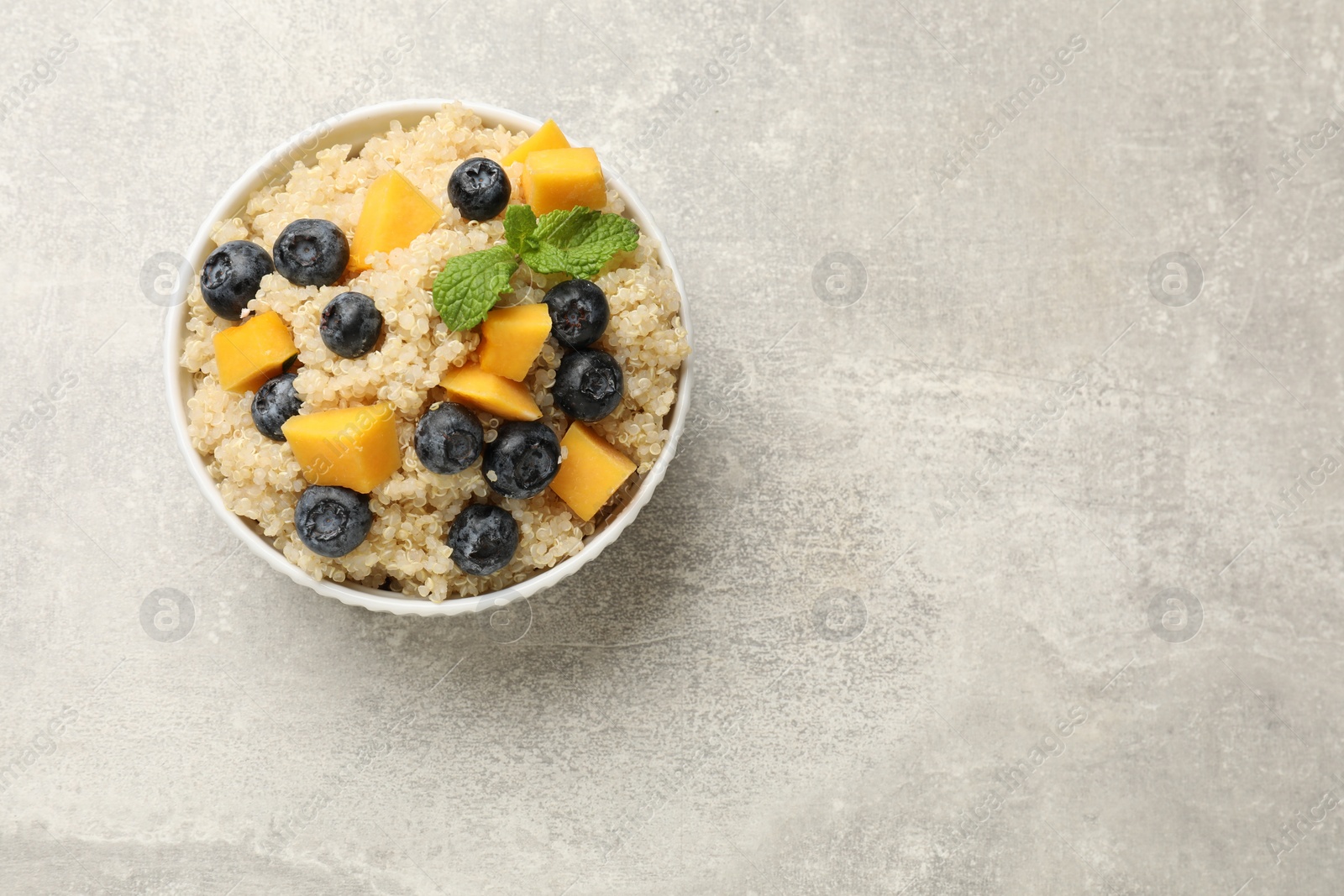 Photo of Tasty quinoa porridge with blueberries and pumpkin in bowl on light grey table, top view. Space for text