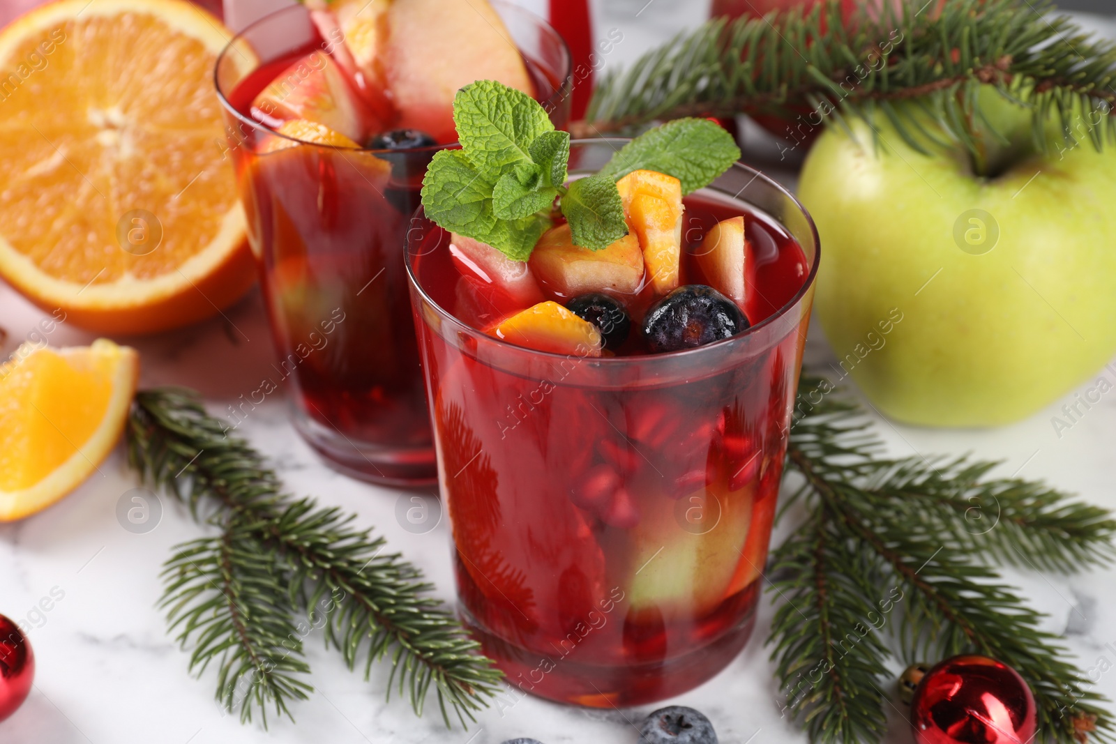 Photo of Aromatic Sangria drink in glasses, ingredients and Christmas decor on white marble table