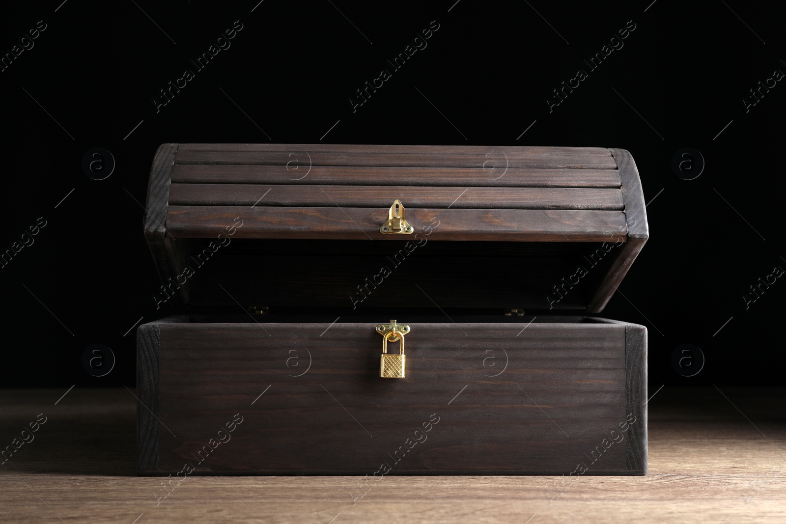 Photo of Open treasure chest on wooden table against black background