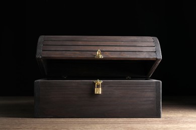 Photo of Open treasure chest on wooden table against black background