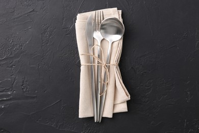 Set of stylish cutlery and napkin on black table, top view