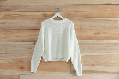 Photo of Hanger with stylish sweater on wooden wall