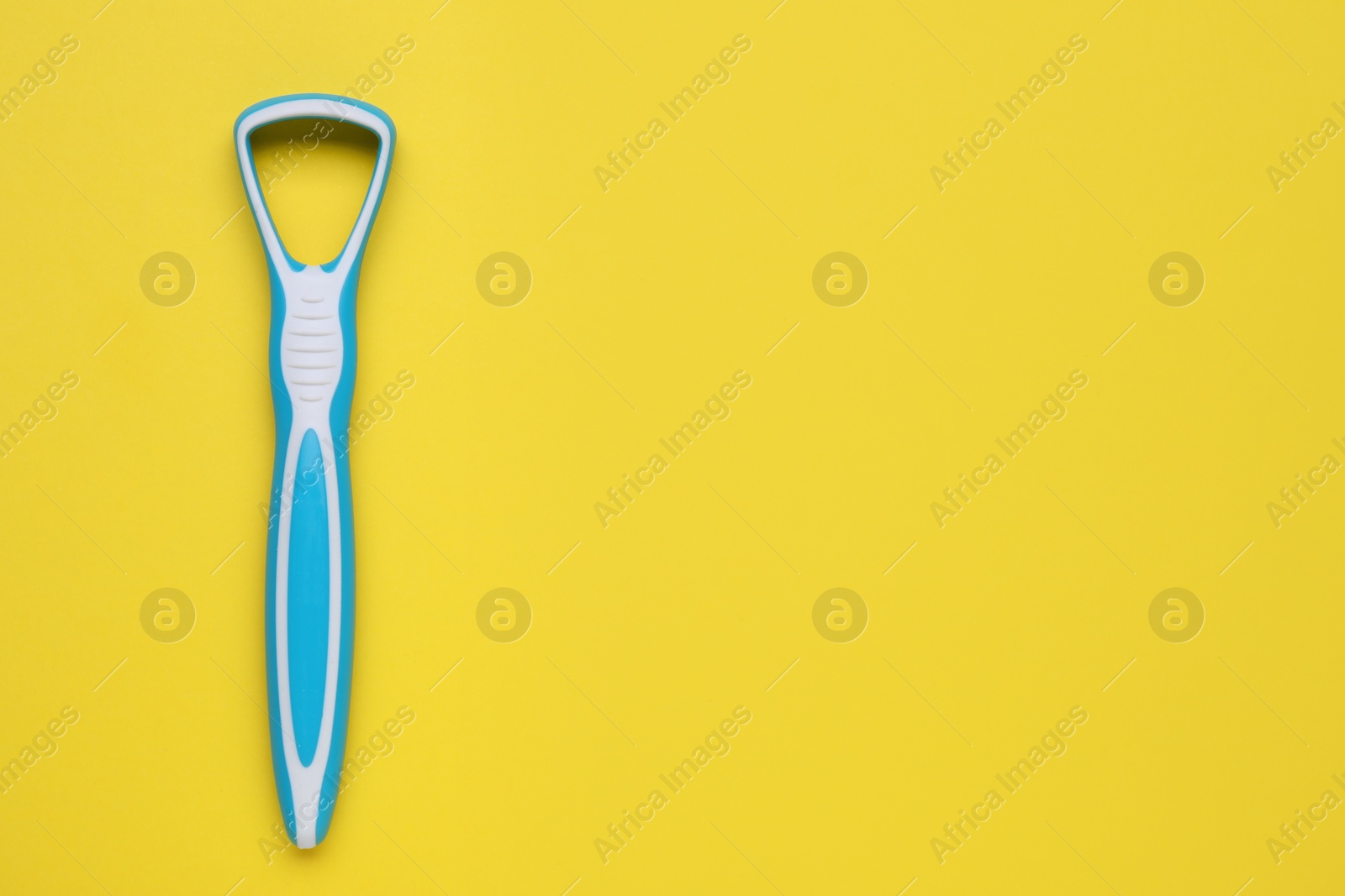 Photo of Light blue tongue cleaner on yellow background, top view. Space for text