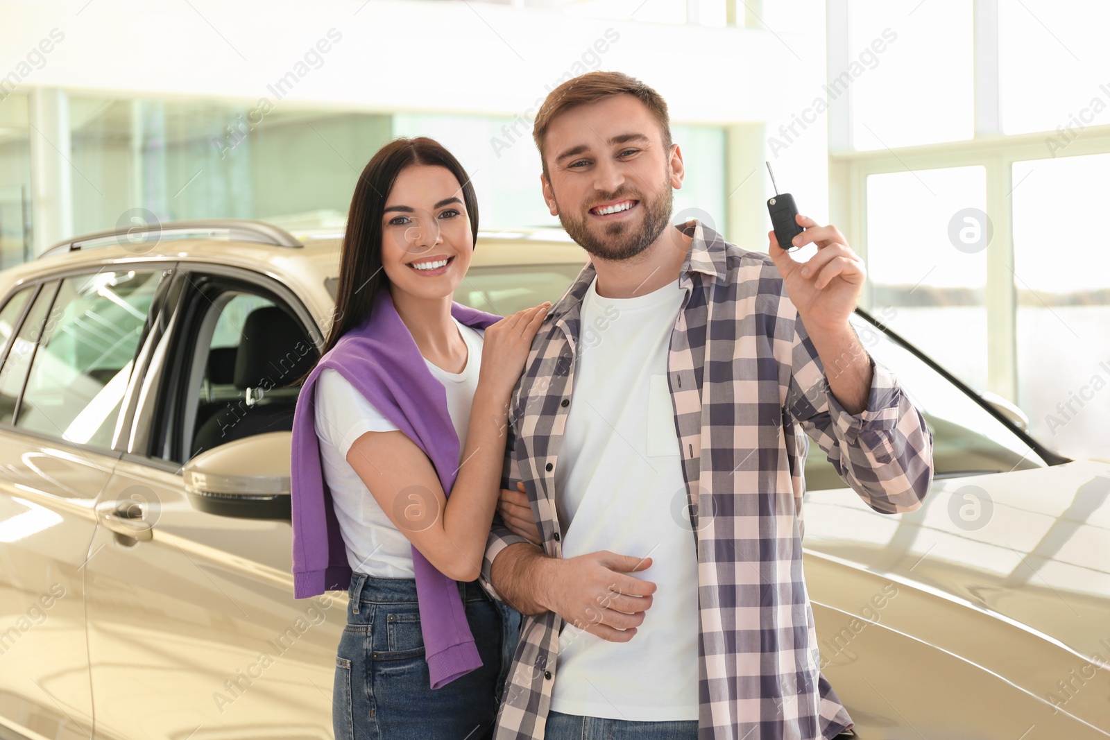 Photo of Happy couple with car key in modern auto dealership