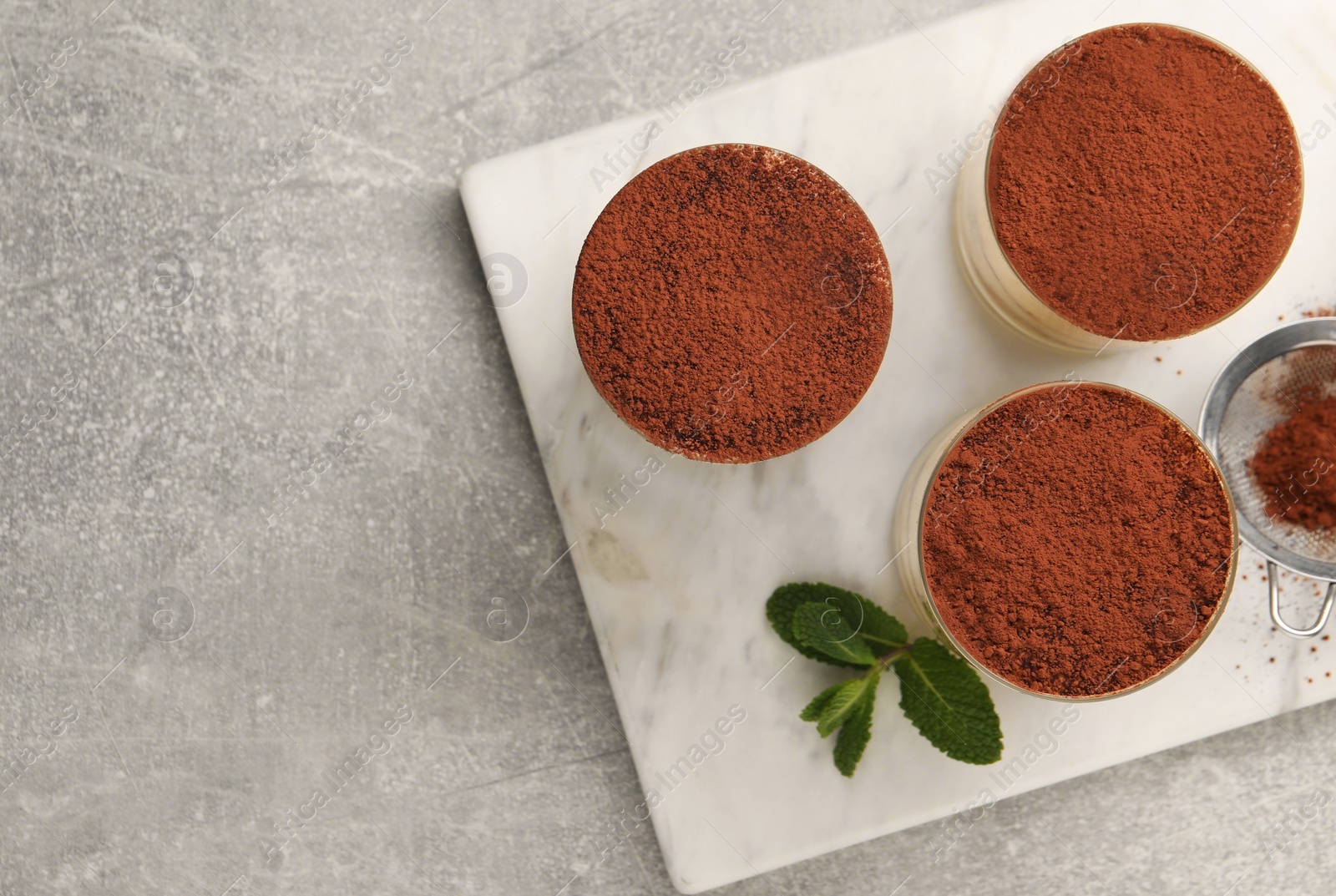 Photo of Delicious tiramisu in glasses and mint on grey textured table, top view. Space for text