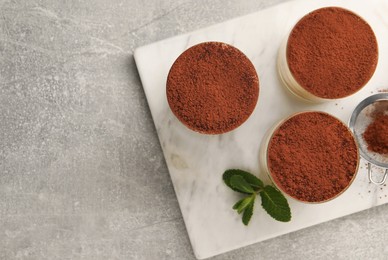 Delicious tiramisu in glasses and mint on grey textured table, top view. Space for text