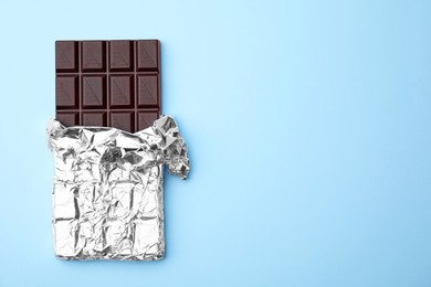Photo of Tasty chocolate bar on light blue background, top view. Space for text