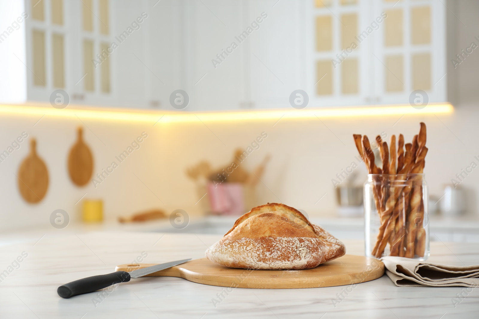 Photo of Loaf of bread, grissini and knife on white table in kitchen. Space for text