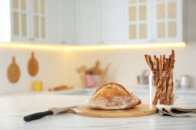 Photo of Loaf of bread, grissini and knife on white table in kitchen. Space for text