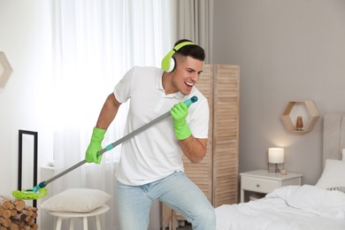 Photo of Man with mop singing while cleaning in bedroom