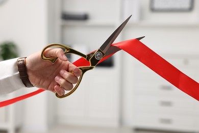 Photo of Woman cutting red ribbon with scissors indoors, closeup