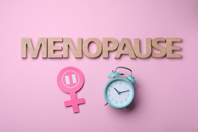 Word Menopause made of wooden letters, female gender sign and alarm clock on pink background, flat lay