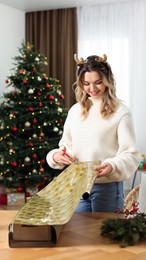 Beautiful young woman wrapping Christmas gift at home