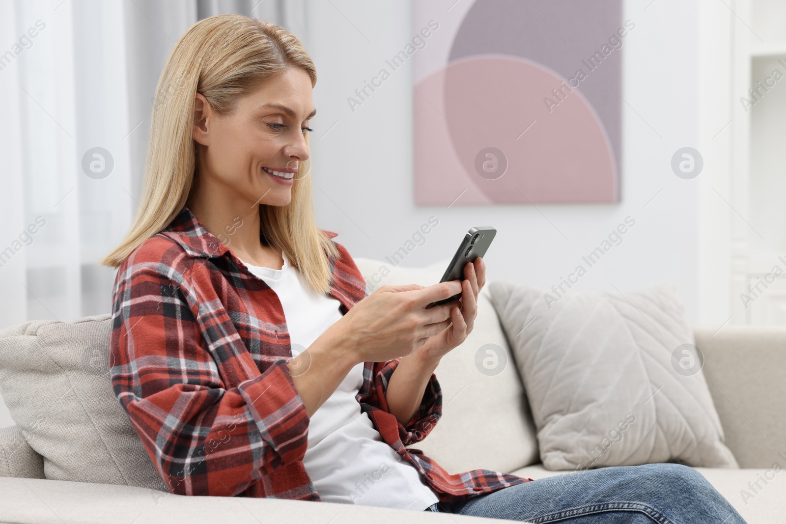 Photo of Happy woman sending message via smartphone on couch at home, space for text