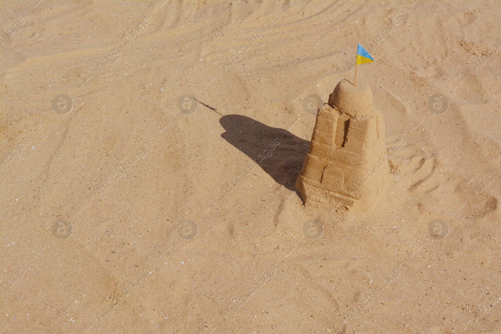 Photo of Beautiful sand castle with small Ukrainian flag on beach, space for text