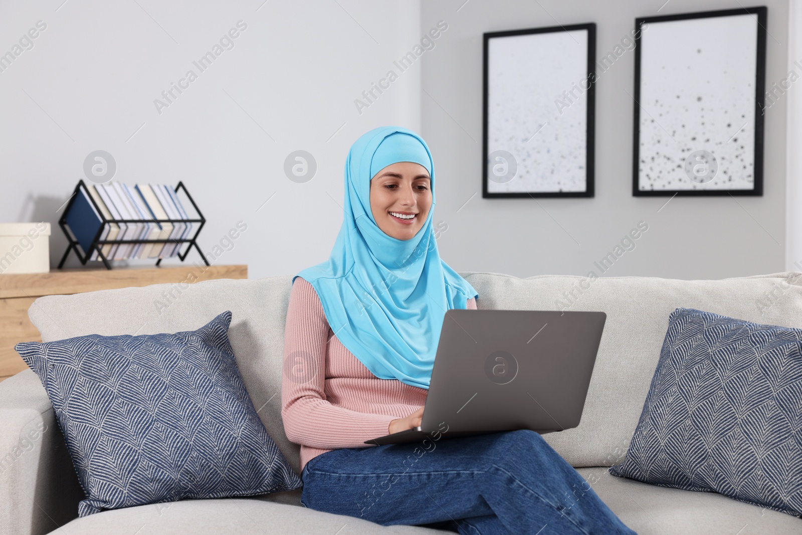 Photo of Muslim woman using laptop at couch in room